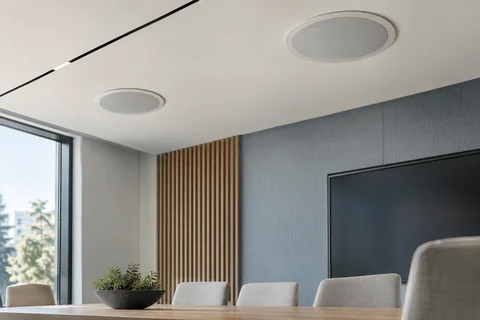 Illustrative a pair of ceiling speakers above a minimalist meeting room
